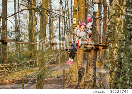 Two adorable little girls in helmet in a rope park in the woods 50222742