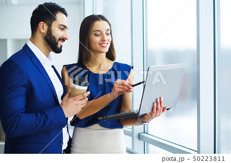 Pretty mixed race woman and her bearded colleague using laptop in order to discuss joint project in 50223811