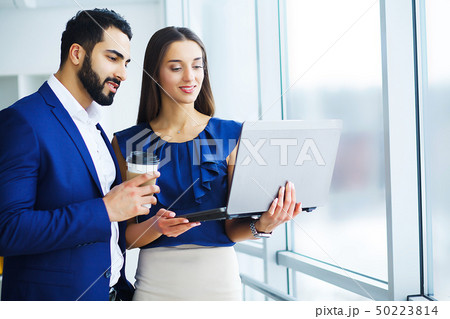 Pretty mixed race woman and her bearded colleague using laptop in order to discuss joint project in 50223814