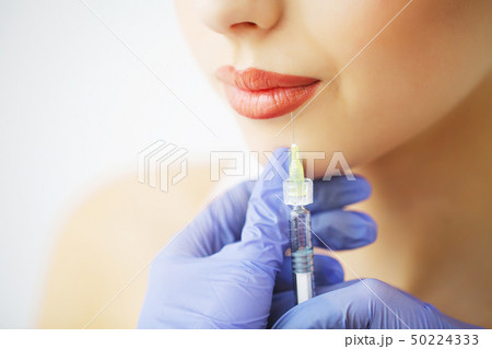 Close up of hands of cosmetologist making botox injection in female lips. She is holding syringe Close up of hands of cosmetologist making botox injection in female lips. She is holding syringe 50224333