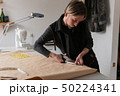 Male fashion designer with scissors cuts paper clothing pattern in workshop 50224341