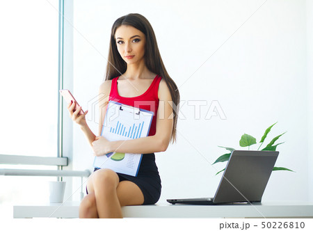 Business. Beautiful Young Woman Works on the Computer. Trims in Hands Phone. Bright Modern Office 50226810