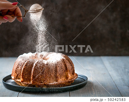 Female hand sprinkling icing sugar on muffin cake 50242583