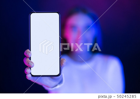 Girl showing blank smartphone screen over neon studio background 50245285