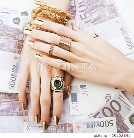 hands of rich woman with golden manicure and many jewelry rings on cash euros close up 50252846