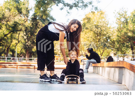 Young mother teaches her little boy to ride a skateboard Young mother teaches her little boy to ride a skateboard 50253063