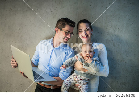A young businessman with wife and baby daughter standing in office, using laptop. 50266109