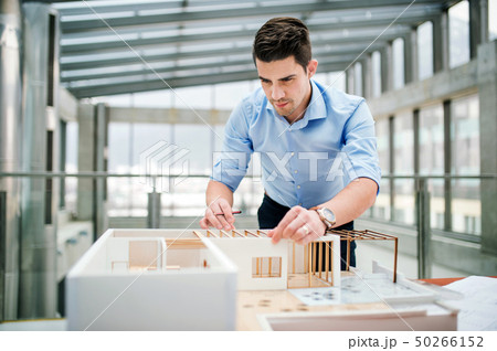Young businessman or architect with model of a house standing in office, working. Young businessman or architect with model of a house standing in office, working. 50266152