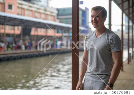 Young happy tourist man thinking while waiting at the local pier in Bangkok 50276695