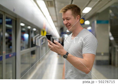 Young happy tourist man using phone at the underground train station in Bangkok 50276715