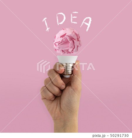 Hand holding paper illuminated light bulb on pink Hand holding paper illuminated light bulb on pink 50291730