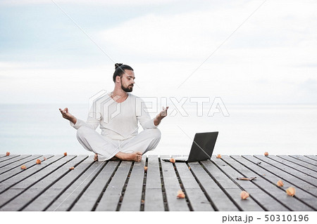 Man in white clothes meditating yoga on wooden pier 50310196