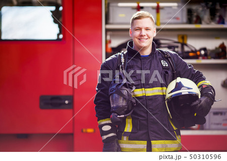 Photo of happy male firefighter with helmet in his hands against background of fire truck 50310596