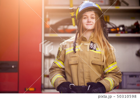 Photo of woman firefighter in helmet standing near fire truck at fire station 50310598
