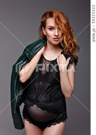 Portrait of the young pregnant woman with red hair in green jacket in the studio on a gray Portrait of the young pregnant woman with red hair in green jacket in the studio on a gray 50325322