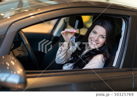 Happy woman buyer examines her new vehicle in car dealership 50325769