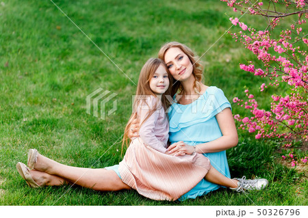 Young beautiful woman with a little daughter walking through the blooming sakura.The concept of 50326796