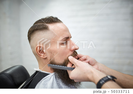 Brutal guy in modern Barber Shop. Hairdresser makes hairstyle a man with a long beard. Master 50333711