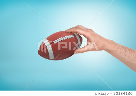 Man's hand holding ball for American football on light blue gradient background. Man's hand holding ball for American football on light blue gradient background. 50334130