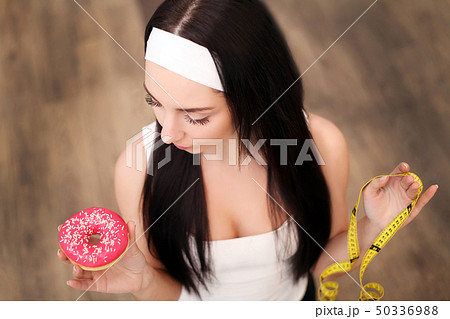 Fit woman in sport clothing holding measuring tape while eating a donut again 50336988