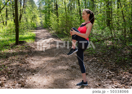Woman runner doing warm-up exercise before jogging in forest Woman runner doing warm-up exercise before jogging in forest 50338066