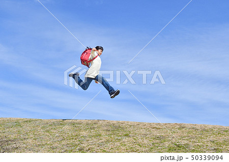 青空でジャンプする小学生の女の子 ランドセル の写真素材