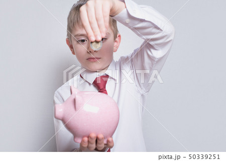 Boy in a shirt and tie puts a coin in a pink piggy Boy in a shirt and tie puts a coin in a pink piggy 50339251
