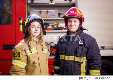 Photo of firefighters women and men in helmets looking at camera near fire truck Photo of firefighters women and men in helmets looking at camera near fire truck 50350222