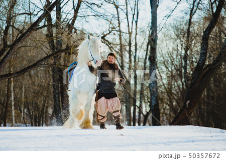 Man in suit of ancient warrior walking with the big white horse 50357672