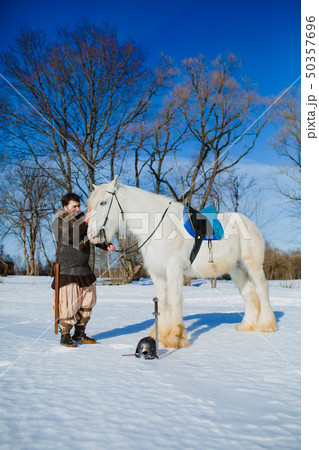 Man in suit of ancient warrior standing near the big white horse 50357696