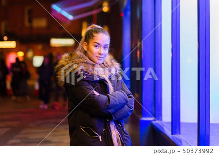 Mixed race teenage with fur coat standing next to window with blue light 50373992
