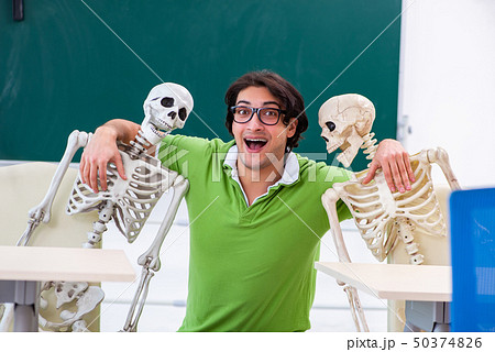 Funny male student in the classroom with skeleton  50374826