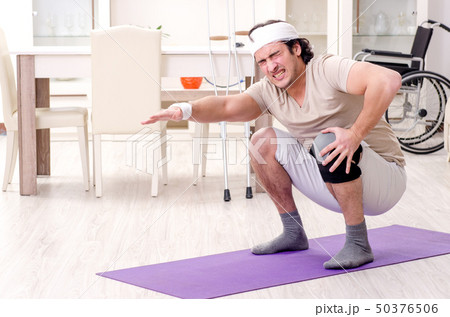 Injured young man doing exercises at home  Injured young man doing exercises at home  50376506