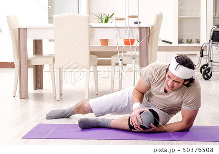 Injured young man doing exercises at home  Injured young man doing exercises at home  50376508