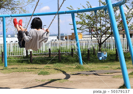 子供 女の子 小学生 ブランコ ぶらんこ 公園 快晴 春 背中 後ろ姿の写真素材
