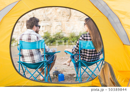 people, summer tourism and nature concept - young couple drinking tea near tent people, summer tourism and nature concept - young couple drinking tea near tent 50389844
