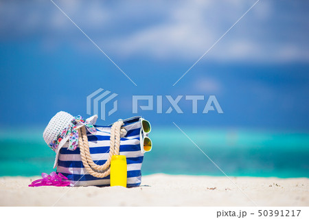 Blue bag, straw white hat, sunglasses, flip flop and sunscreen bottle on tropical beach Blue bag, straw white hat, sunglasses, flip flop and sunscreen bottle on tropical beach 50391217