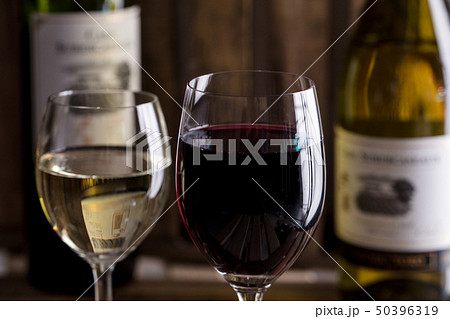 木の背景で赤ワインと白ワインのボトルとワイングラスがオシャレにおいてあるワインバーの写真素材