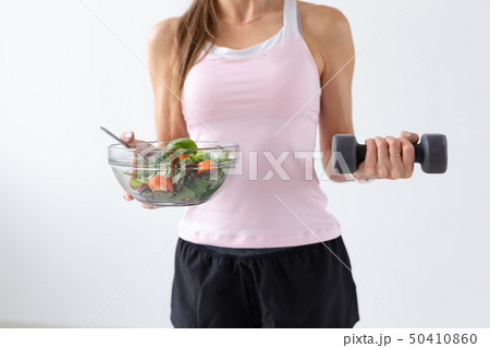 Diet, food and fitness concept - Close up of healthy salad and dumbbell in female hand over white 50410860