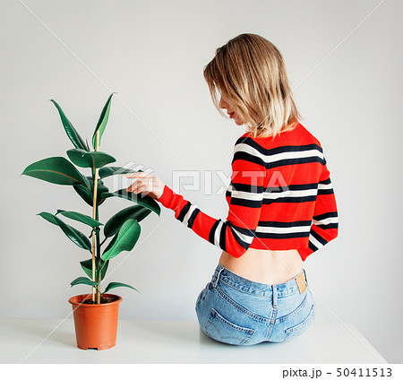 woman in sptriped sweater and jeans sitting on a table near ficus 50411513