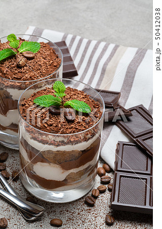 two portions Classic tiramisu dessert in a glass and chocolate bar on concrete background 50412038