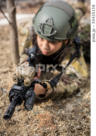 迷彩服を着ている女の子がエアーガンを持ってサバイバルゲームをしている姿 迷彩服を着ている女の子がエアーガンを持ってサバイバルゲームをしている姿 50420158