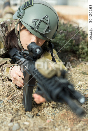 迷彩服を着ている女の子がエアーガンを持ってサバイバルゲームをしている姿 迷彩服を着ている女の子がエアーガンを持ってサバイバルゲームをしている姿 50420163