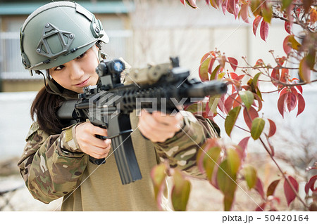 迷彩服を着ている女の子がエアーガンを持ってサバイバルゲームをしている姿 50420164