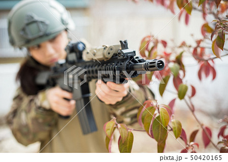 迷彩服を着ている女の子がエアーガンを持ってサバイバルゲームをしている姿 50420165