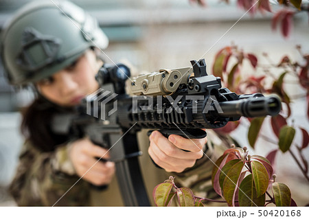 迷彩服を着ている女の子がエアーガンを持ってサバイバルゲームをしている姿 50420168