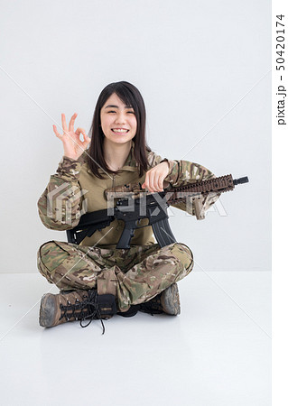 白背景に迷彩服を着てエアガンを持っている笑顔も女の子が指で丸を差している 白背景に迷彩服を着てエアガンを持っている笑顔も女の子が指で丸を差している 50420174