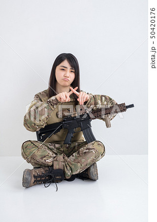 白背景に迷彩服を着てエアガンを持っている笑顔も女の子が指でバツを差している 50420176