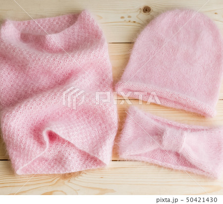 A set of caps, necks and headbands knitted by hand from pink Angora, on wooden background 50421430
