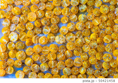 Cut the yellow cherry tomatoes sprinkled with spices on white parchment prepared for drying Cut the yellow cherry tomatoes sprinkled with spices on white parchment prepared for drying 50421458